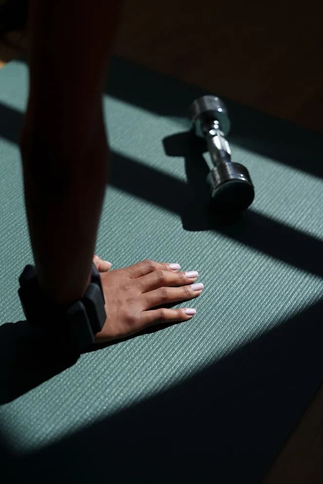 Hand on a training mat next to a dumbbell